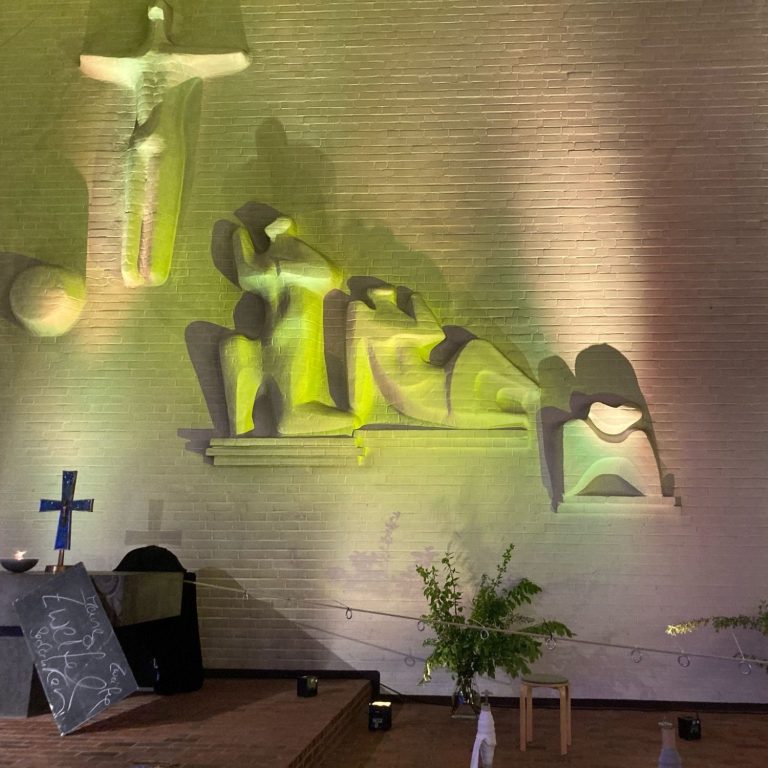 Künstlerische Darstellung eines Kreuzes und stilisierter Figuren in sanften Lichttönen.