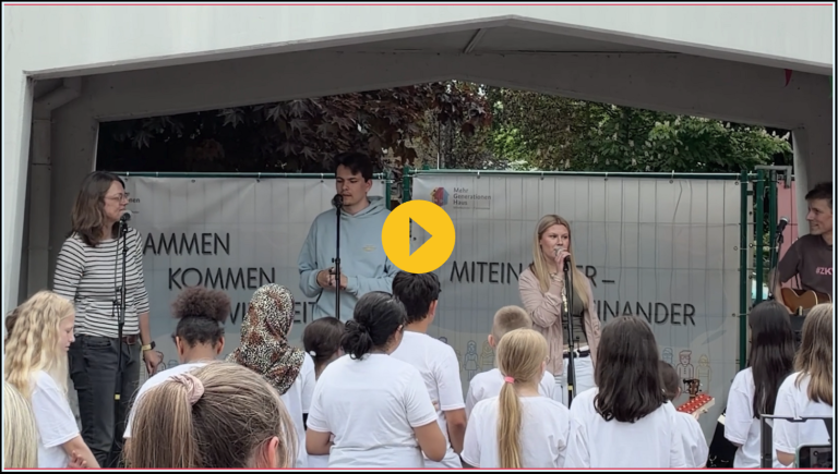 Vier Sänger stehen auf einer Bühne, vor ihnen eine Gruppe von Zuhörern in weißen T-Shirts.
